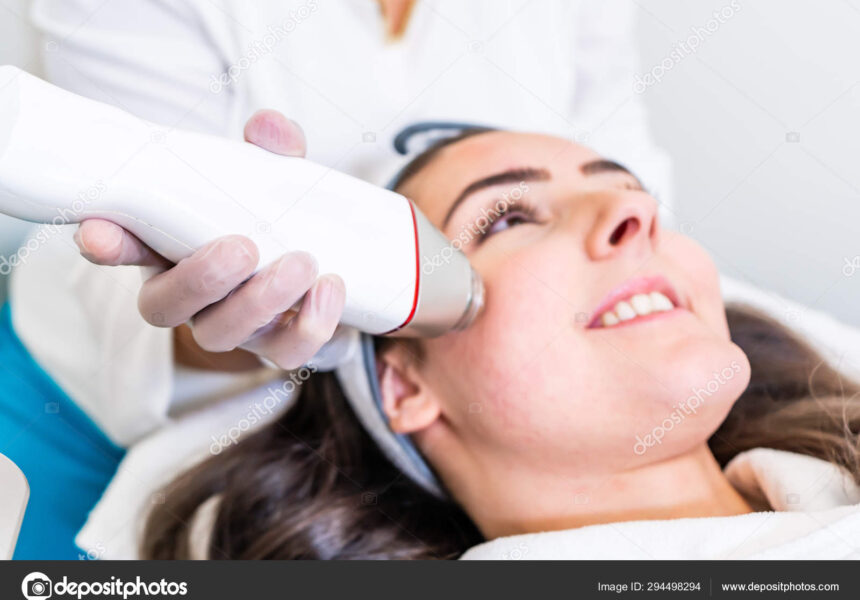 Radio frequency microneedling machine handpiece on the cheek of a woman's face during a beauty skin tightening treatment.